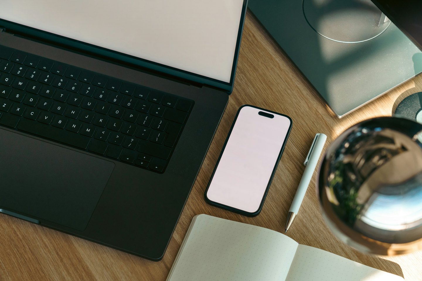 Laptop, notebook, and smartphone arranged on a wooden desk.